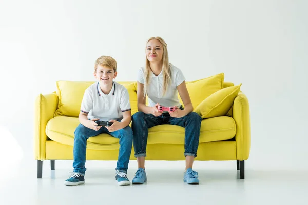 Alegre madre e hijo jugando video juego en amarillo sofá en blanco - foto de stock