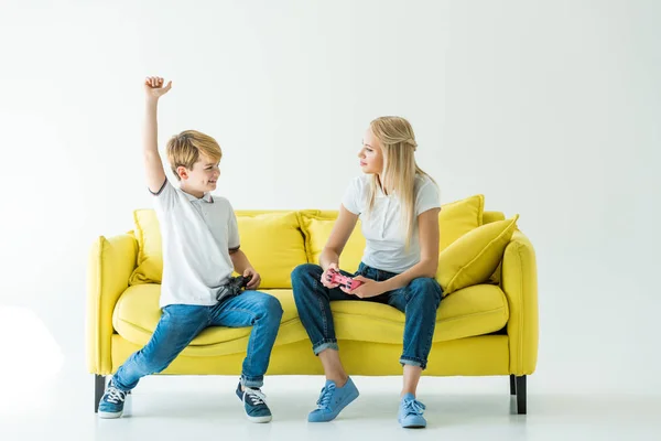 Glücklicher Sohn zeigt Ja-Geste nach gewonnenem Videospiel auf gelbem Sofa auf weißem — Stockfoto