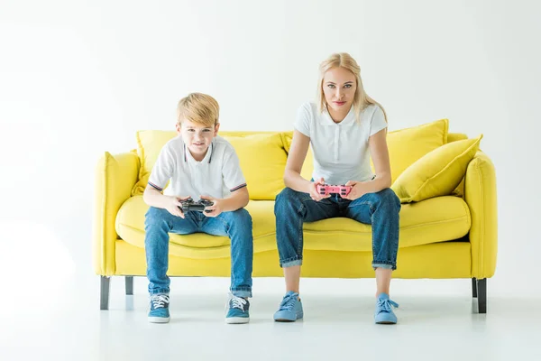 Серйозна мати і син грають у відеогру на жовтому дивані на білому — стокове фото