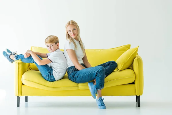 Mère et fils assis dos à dos sur canapé jaune sur blanc — Photo de stock