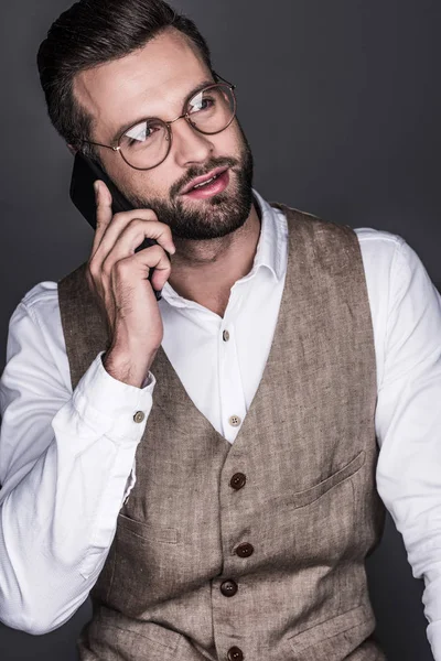 Retrato de hombre barbudo guapo posando en gafas hablando en smartphone, aislado en gris - foto de stock