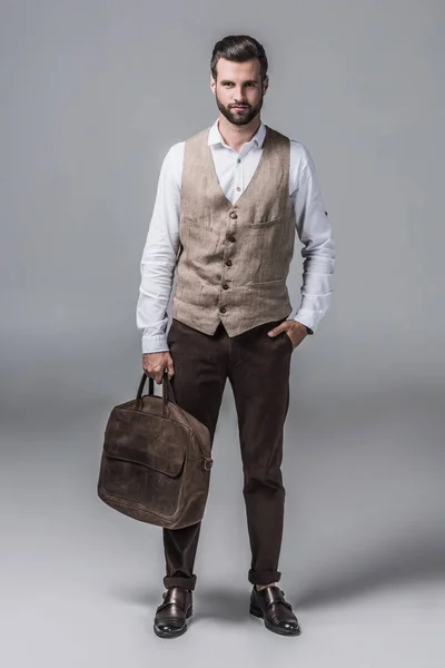 Красивый элегантный мужчина позирует с кожаной сумкой на сером — стоковое фото