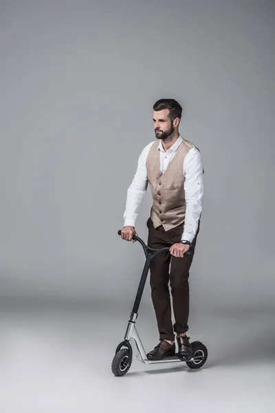 Handsome elegant man in trendy waistcoat riding modern scooter on grey — Stock Photo