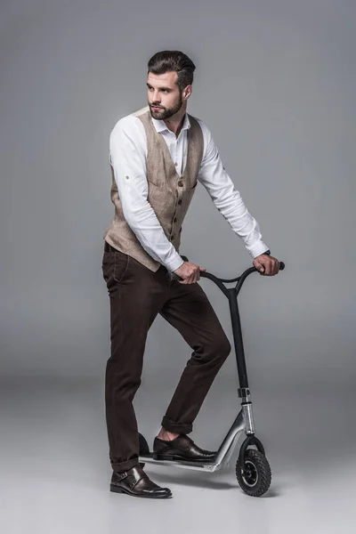 Stylish elegant young man posing on modern scooter on grey — Stock Photo
