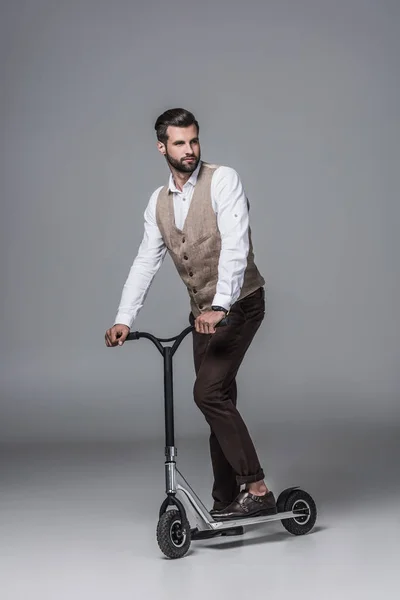 Stylish elegant bearded man on modern scooter on grey — Stock Photo
