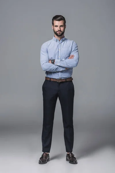 Confiado hombre de negocios elegante posando con los brazos cruzados, en gris - foto de stock