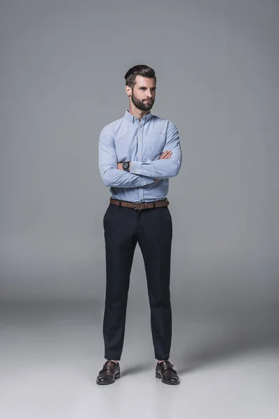 Bell'uomo d'affari sicuro in piedi con le braccia incrociate, su grigio — Foto stock