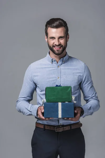Sonriente hombre de negocios elegante sosteniendo cajas de regalo, aislado en gris - foto de stock