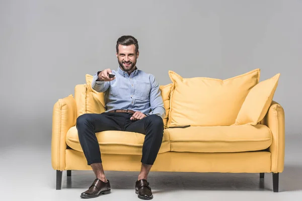 Homme d'affaires joyeux avec télécommande regarder la télévision sur canapé jaune sur gris — Photo de stock