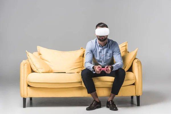 Geschäftsmann spielt Videospiel mit Steuerknüppel und Vr-Headset auf gelbem Sofa auf grau — Stockfoto