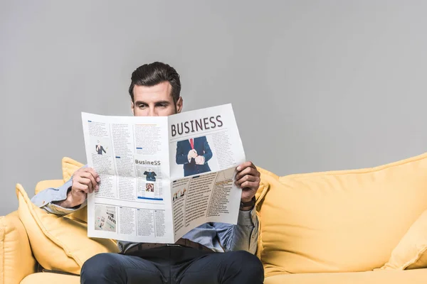 Homme d'affaires barbu lisant un journal d'affaires assis sur un canapé, sur du gris — Photo de stock