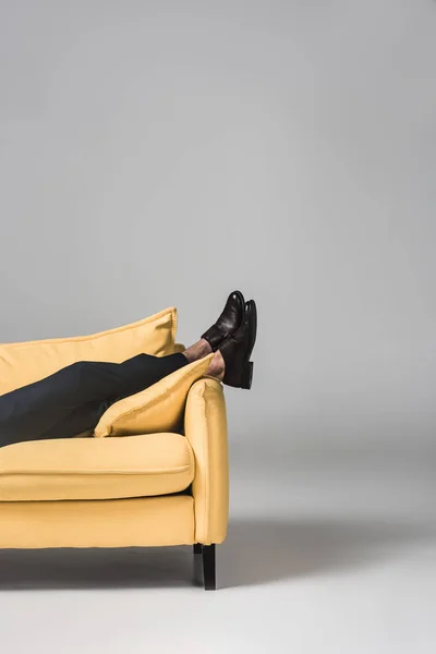 Vista recortada de piernas masculinas tumbadas en sofá amarillo sobre gris - foto de stock