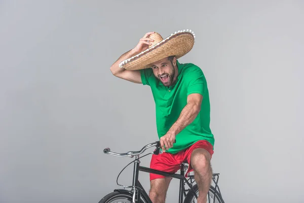 Збуджений чоловік в мексиканському сомбреро їзда на велосипеді на сірому — стокове фото