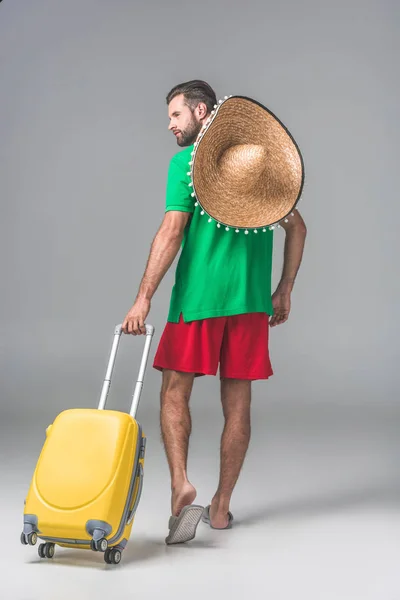 Back view of male tourist in mexican sombrero walking with travel bag on grey — Stock Photo