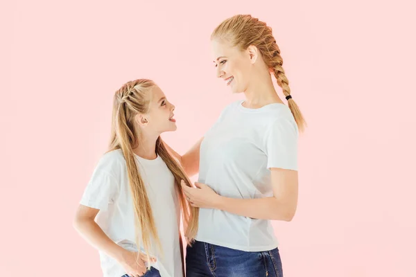 Feliz joven madre e hija en camisetas blancas mirándose aisladas en rosa - foto de stock