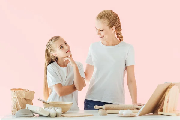 Happy mother and daughter in white t-shirts having fun together while cooking isolated on pink — Stock Photo