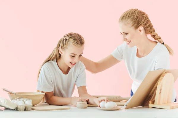 Felice giovane madre e figlia in bianco t-shirt cucina insieme isolato su rosa — Foto stock