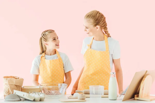 Happy mother and daughter looking at each other while preparing dough isolated on pink — Stock Photo