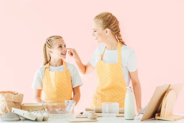 Madre e hija jugando con harina mientras preparan masa aislada en rosa - foto de stock