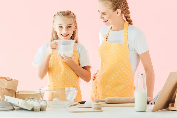 Happy mother and daughter with ingredients cooking together isolated on pink — Stock Photo