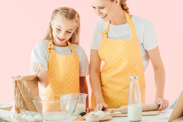 Happy attractive mother and daughter with flour cooking together isolated on pink — Stock Photo