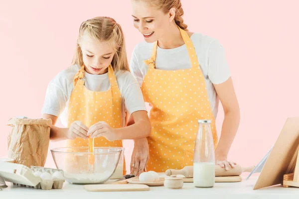 Smiling young mother teaching daughter how to knead dough isolated on pink — Stock Photo