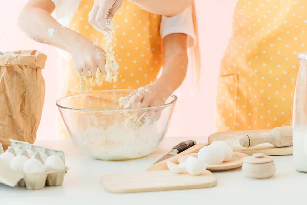Cropped shot of mother and daughter preparing dough in glass bowl together isolated on pink — Stock Photo
