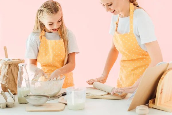 Счастливая молодая мать и дочь смешивая тесто вместе изолированы на розовый — стоковое фото