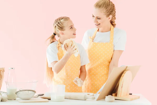 Glückliche junge Mutter und Tochter kneten Teig zusammen isoliert auf rosa — Stockfoto