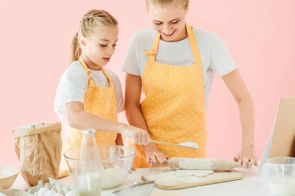 Mother and cute little daughter preparing dough together isolated on pink — Stock Photo