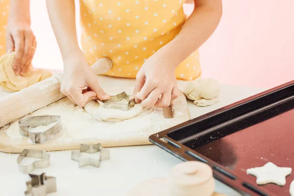 Schnappschuss eines kleinen Mädchens, das mit Mutter Teig in verschiedenen Formen für Plätzchen schneidet — Stockfoto