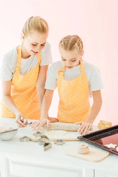 Belle jeune mère et fille préparant la pâte pour les biscuits de vacances ensemble isolé sur rose — Photo de stock