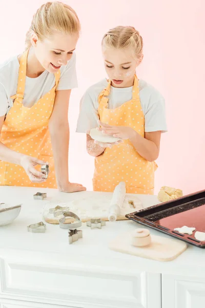 Счастливая молодая мать и дочь готовят тесто для праздника печенье вместе изолированы на розовый — стоковое фото