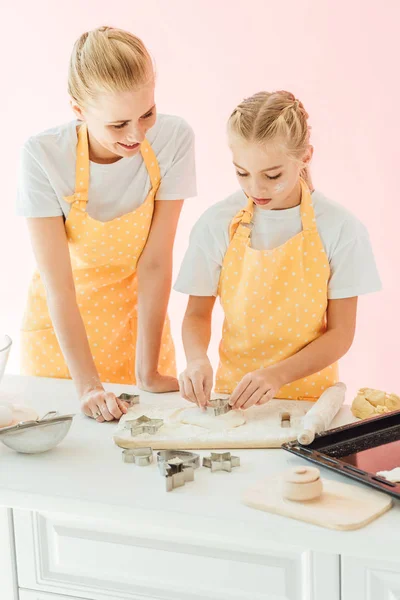 Young mother and daughter preparing dough for holiday cookies together isolated on pink — Stock Photo
