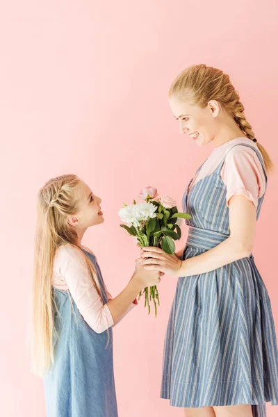 Glückliche junge Mutter und Tochter halten schönen Strauß in der Hand und betrachten einander isoliert auf rosa — Stockfoto