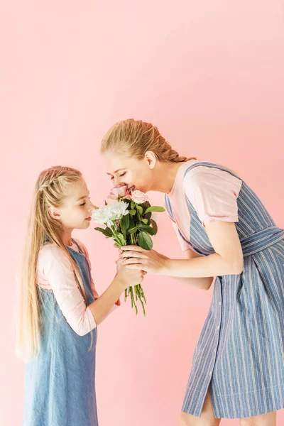 Happy young mother and daughter sniffing bouquet together isolated on pink — Stock Photo