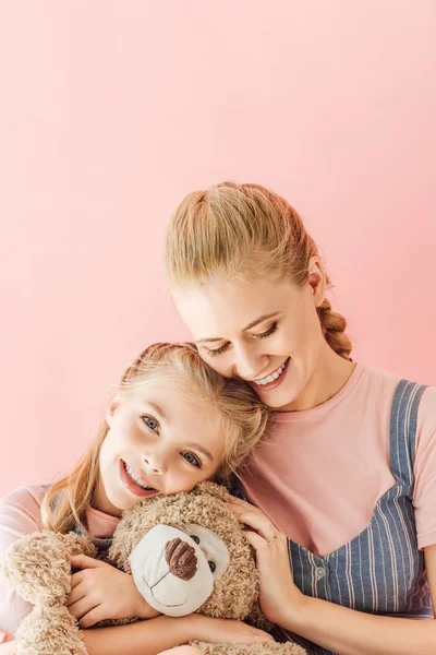 Beautiful happy mother and daughter with teddy bear isolated on pink — Stock Photo
