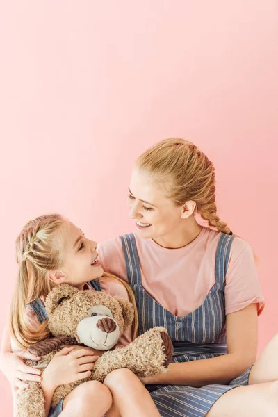 Мати і дочка з плюшевим ведмедем обіймаються і дивляться один на одного ізольовані на рожевому — стокове фото