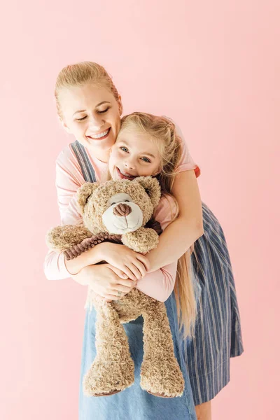 Щаслива мати і дочка з плюшевим ведмедем, що обіймається ізольовано на рожевому — стокове фото