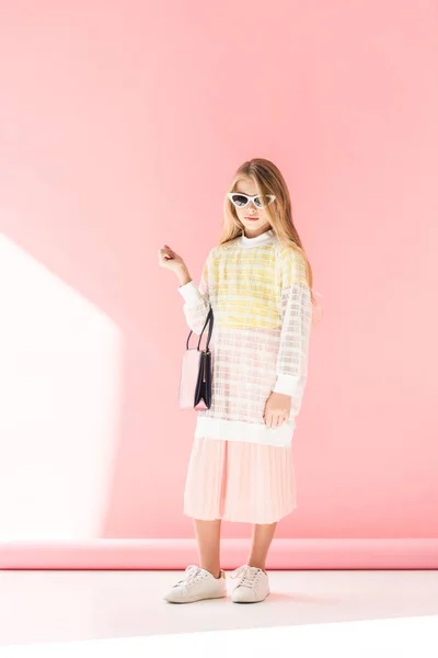 Elegante joven en gafas de sol posando con bolso de moda en rosa - foto de stock