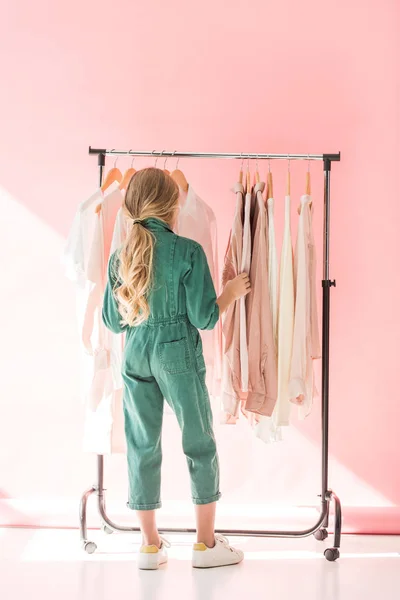 Back view of kid in trendy overalls choosing clothes on hangers — Stock Photo