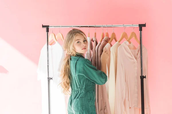 Attractive female child in trendy overalls choosing clothes on hangers — Stock Photo