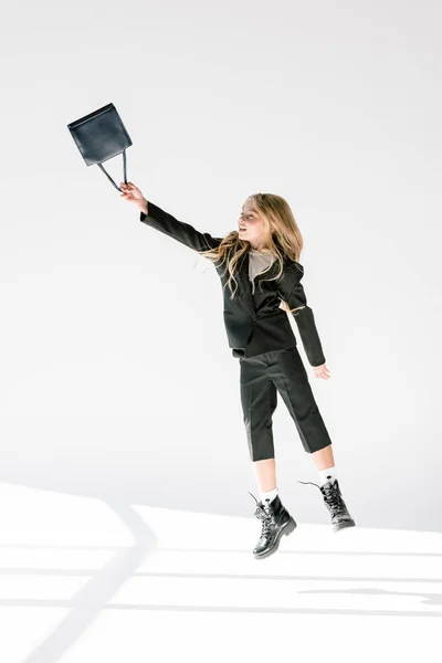 Fashionable child in black suit flying with bag on grey — Stock Photo