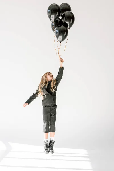 Мечтательный ребенок прыгает или летает с черными воздушными шарами на сером — стоковое фото