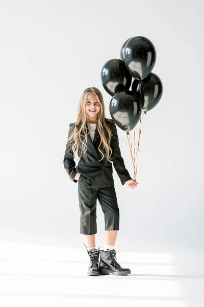 Elegante niña sonriente posando con globos negros sobre gris - foto de stock