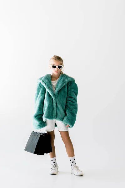 Fashionable kid in turquoise fur coat posing with black shopping bags isolated on white — Stock Photo