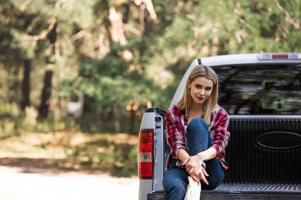 Happy beautiful girl looking at camera and sitting on pickup truck in forest — Stock Photo