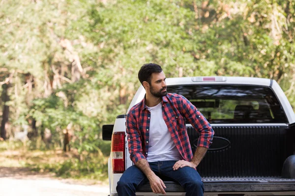 Confident bearded man sitting on pickup truck in forest — Stock Photo