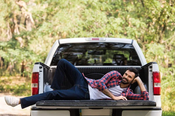 Glücklicher bärtiger Mann entspannt sich auf Pickup-Truck im Wald — Stockfoto