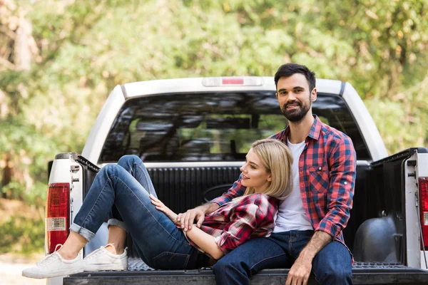 Hermosa pareja sonriente descansando en camioneta en el bosque - foto de stock